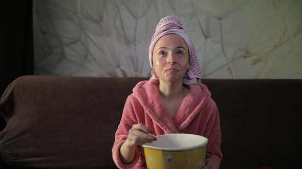 Woman Watching a Late Night Movie at TV, Eating Popcorn. Bathrobe, Facial Mask