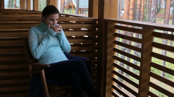 Girl In a Blue Sweater Sitting On a Wooden Chair And Drinking Tea