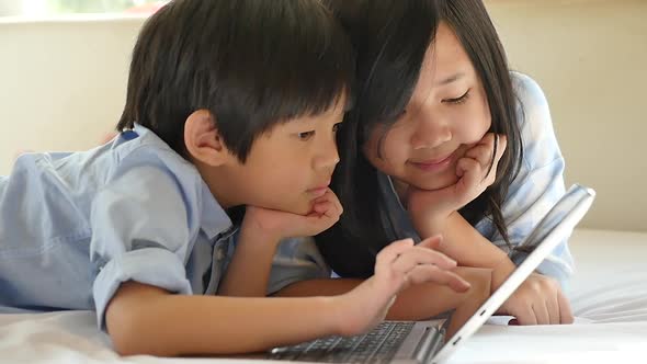 Cute Asian Children  Lying In Bed And Using Laptop On White Bed