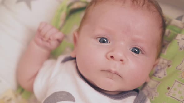 Newborn Baby in Bodysuit Lies in Cocoon in Bedroom Closeup