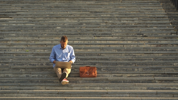 Side View Of Young Man Sitting On The Stairs In Park Using Laptop