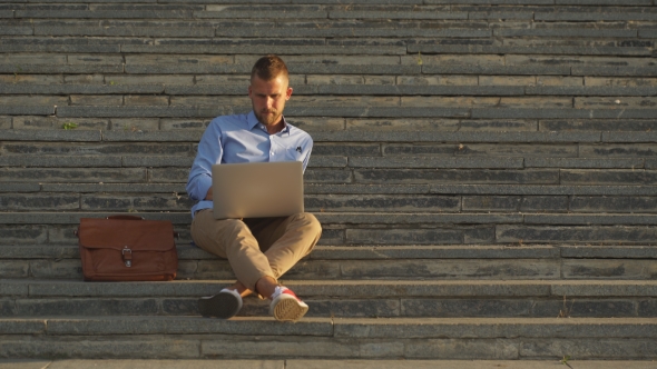 Attractive Businessman Sitting On a College Campus With Laptop Computer