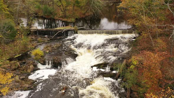 An drone view over a waterfall surrounded by colorful fall foliage in upstate NY. The camera, facing