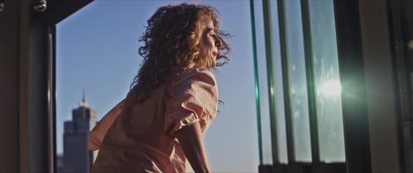 A curly happy woman enjoying the wind and the sun from the balcony