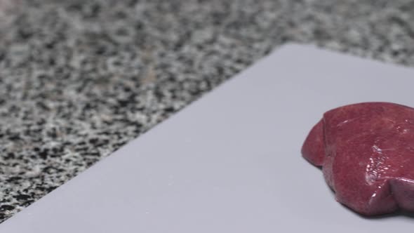 A Chef Slices Raw Pork Liver on a Plastic Board