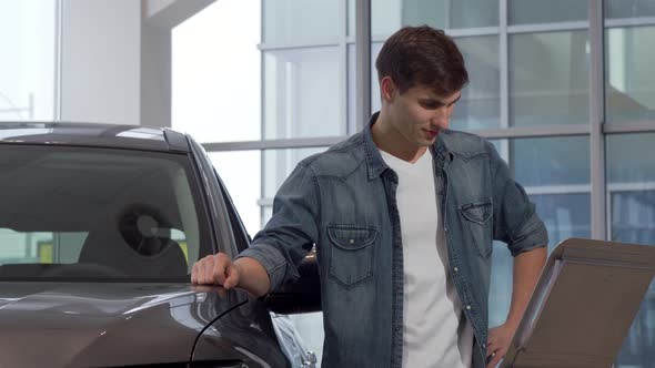 Handsome Man Reading Info Paper at Car Dealership, Choosing New Auto