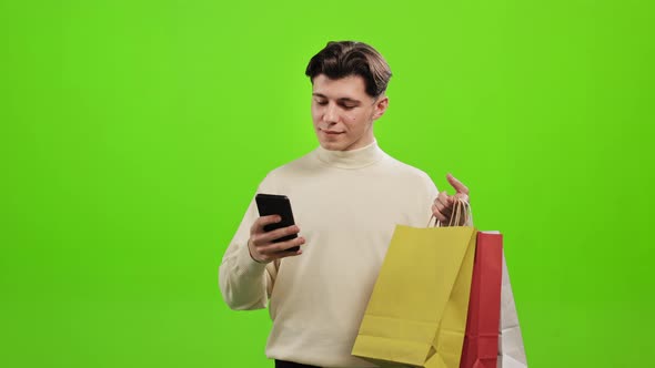 A Man is Texting on a Smartphone and Holding Shopping Bags in His Hands