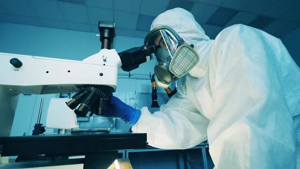 Specialist in a Splash Suit is Working with a Microscope in the Laboratory