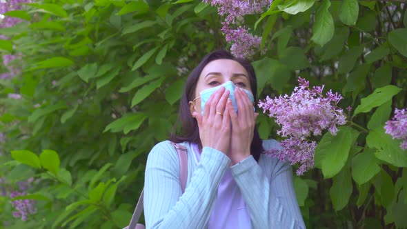 Portrait of Young Allergic Woman in Medical Mask Sneezes and Looks at Camera