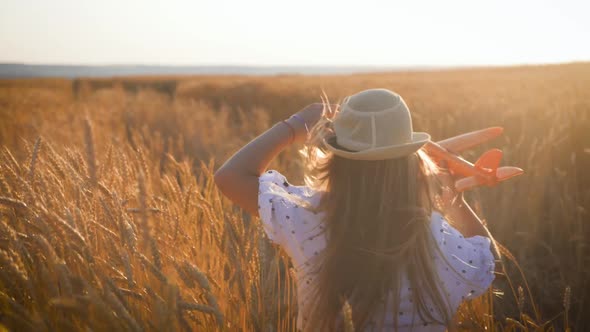 Happy Little Girl Playing with Airplane on a Wheat Field During Sunset. Concept Big Child Dream.