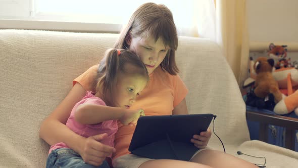 Two Girls Children Sister At Home On Couch Playing On Tablet