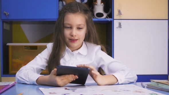 Cute Little Girl Studying At The Library Doing Homework With Tablet