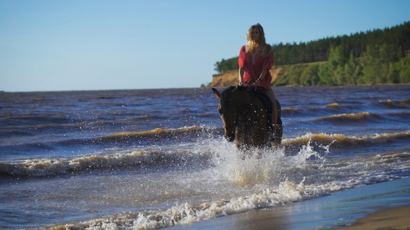 A Beautiful Blonde Young Woman Riding a Horse At a Lake