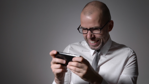 Very Expressive And Emotional Manager In White Shirt And Tie Playing Games On His Smartphone.