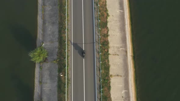 Top View to Motorcyclist Racing His Motorcycle on Road Near Lake or Pond