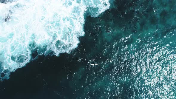 Aerial shot looking directly down at some surfers on the ocean. Wave breaks at the end of clip and t
