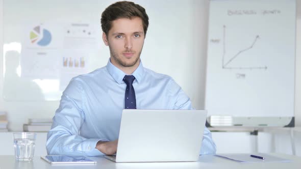 Thumbs Up by Young Businessman Sitting at Desk in Office