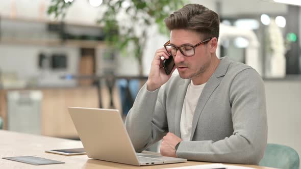 Middle Aged Man with Laptop Talking on Smartphone 