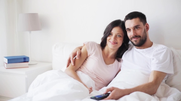 Happy Couple Watching Tv In Bed At Home