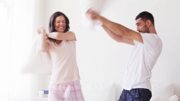 Happy Couple Having Pillow Fight In Bed At Home