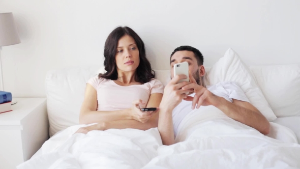 Happy Couple With Smartphones In Bed