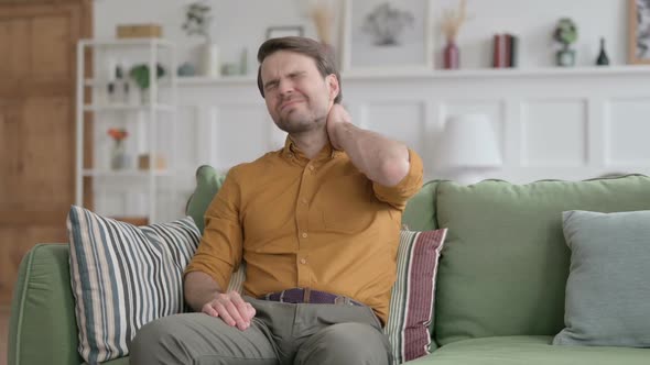 Young Man having Neck Pain while Sitting on Sofa