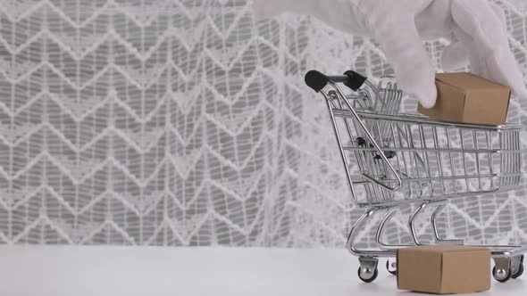 Human Hand in White Cotton Glove Puts Carton Boxes in Mini Shopping Cart