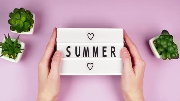 Hands of a young girl grip a white board with the inscription Summer and hearts on a pink background