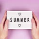 Hands of a young girl grip a white board with the inscription Summer and hearts on a pink background - VideoHive Item for Sale