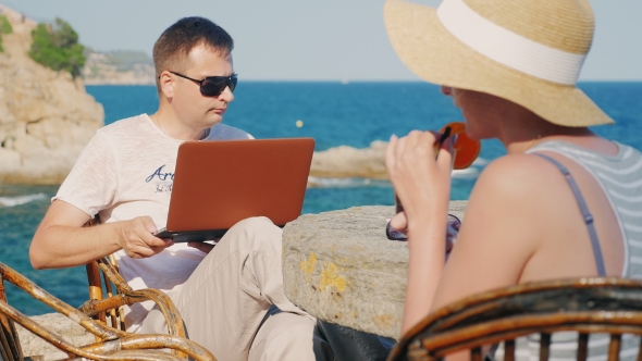 The Couple at the Resort. Woman Drinking Cocktail, Man Working With a Laptop