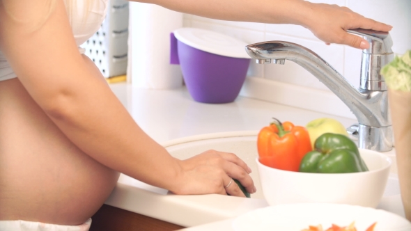 Pregnant Woman Washing Peppers In The Kitchen. Vegetables For Salad