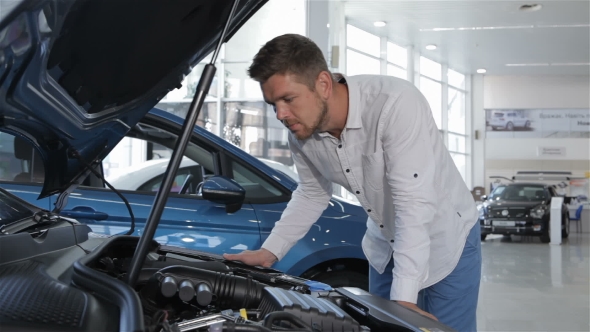 Man Looks at the Engine Compartment of the Car at the Dealership