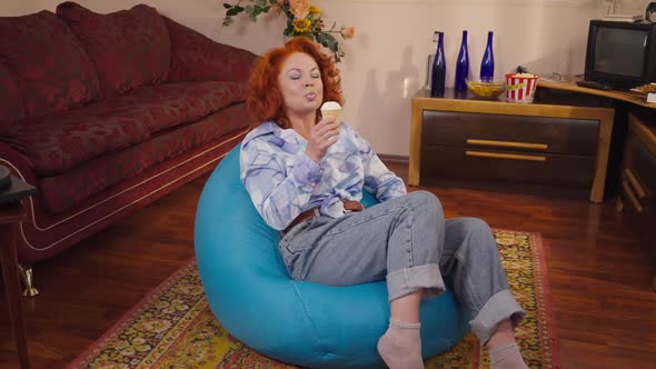 Zoom in Relaxed Caucasian Retro Woman Eating Ice Cream in Slow Motion Sitting on Bag Chair