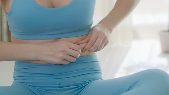 Closeup view of woman in blue sportswear touching her stomach and  gaining weight at home