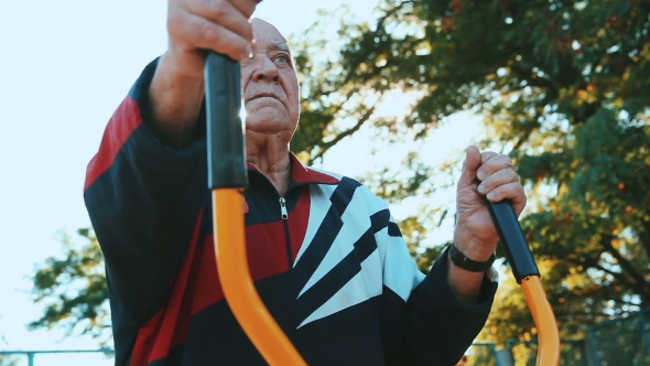 Elderly Man Exercising With Fitness Equipment In Public Outdoor Gym.