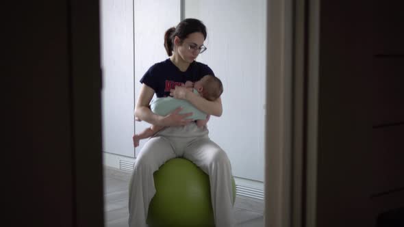 A Young Mother Rocks Her Baby on a Fitness Ball