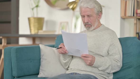 Old Man Reading Documents on Sofa