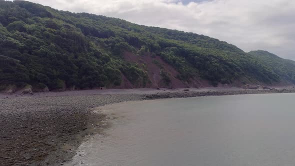 Aerial wide tracking upwards over the sea at the coastline to the west of Porlock Weir, Somerset, En