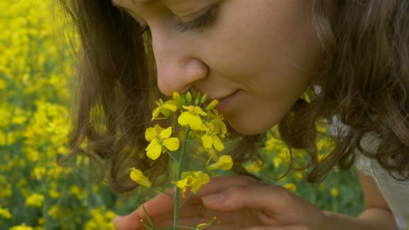 Nice Woman with Brown Curly Hair Sniffs Beautiful Canola