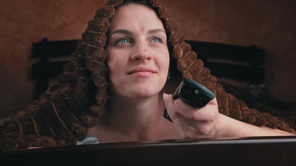 Girl Lying on Bed Watches TV and Switches Channels with Remote Control Closeup