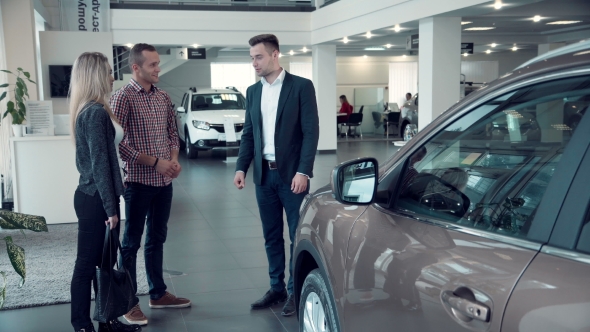 Salesman Talking To Couple Inside Car Dealership