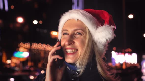 a woman chatting on her smartphone wearing a Santa hat is a night city.