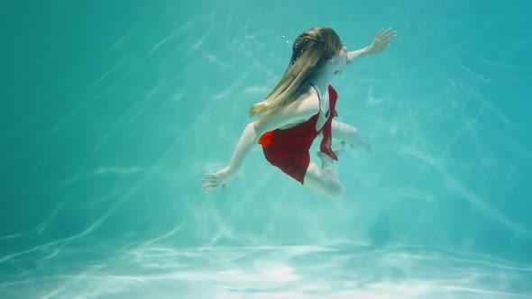 Young Woman in Red Chiffon Costume Dancing Underwater in Blue Water Column with Glare