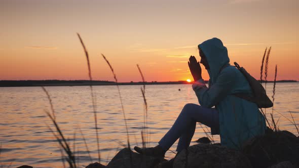 A Lonely Woman Sits on a Rock Near a Picturesque Lake at Sunset