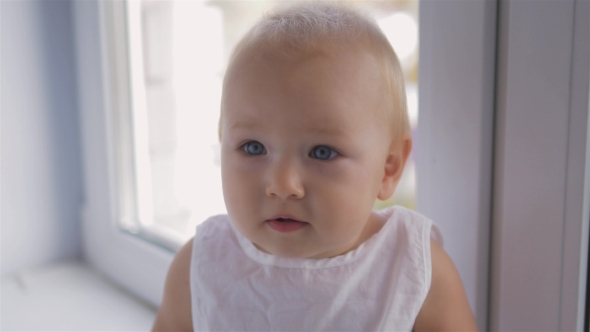 Cute Little Baby Girl Looking Into The Camera And Seat Near Window alt