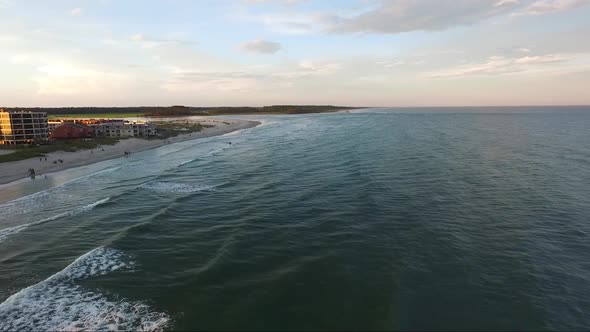 Drone flying over ocean towards inlet at sunset