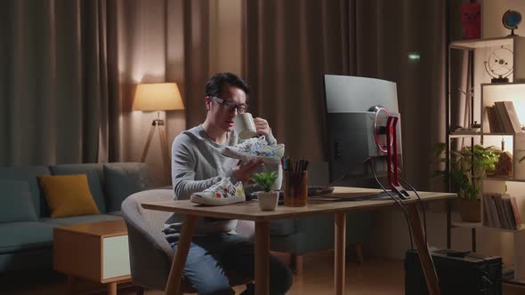 Asian Male Footwear Designer Drinking Coffee While Working On A Desktop Computer At Home