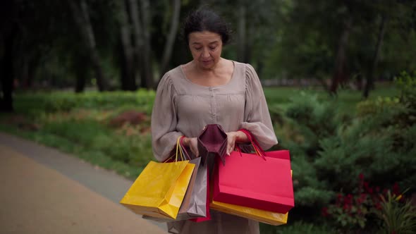 Embarrassed Caucasian Senior Shopper with Shopping Bags Opening Empty Wallet Looking at Camera with