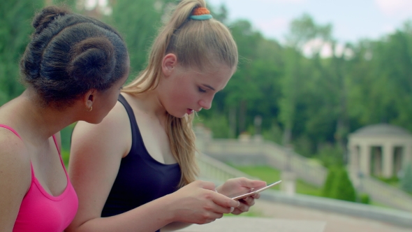 Blonde Girl Showing Photos On Tablet To African Girlfriend