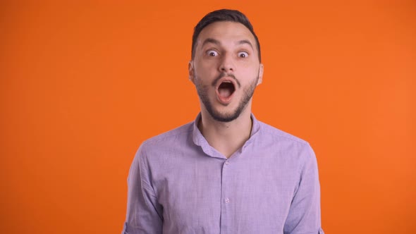 Young Excited Man Touching Head with Hands Over Orange Studio Background